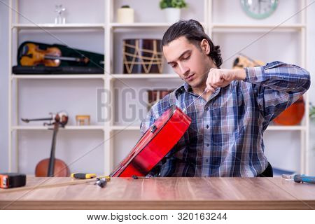 Young handsome repairman repairing guitar
