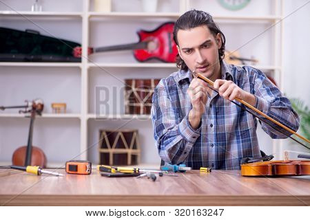 Young handsome repairman repairing violin
