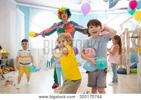 Clown At Children Birthday Party Entertaining Group Of Kids. Children Play With Ballons