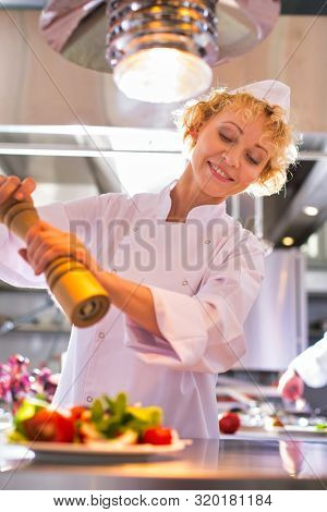 Mature chef using peppermill on salad in plate at restaurant