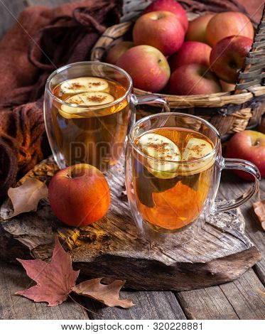 Two Cups Of Apple Cider With Apple Slices Sprinkled With Cinnamon On A Rustic Wooden Surface And Bas