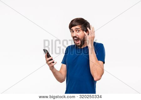 Pretty Brunet Man In A Blue Shirt With Beard And Mostaches Shocked Holding Smartphone Looking At The