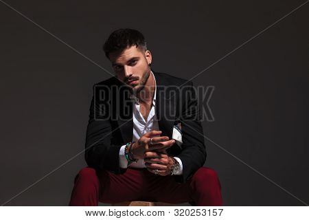 seated elegant man rubbing his palms and shows his rings on grey background