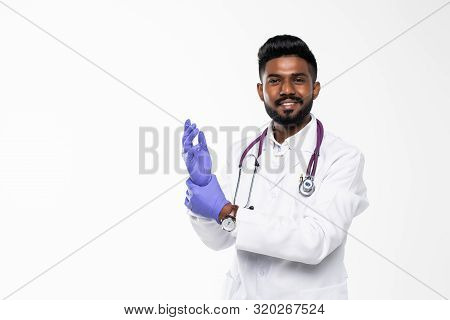 Indian Doctor Or Physician Male Looking At Hand With Focused Expression As Putting On Blue Surgical 