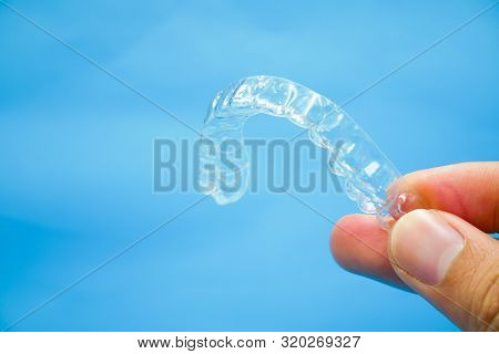 Hand Holding Clear Plastic Retainer Teeth That Isolated On Blue Sky Background. It's An Equipment Fo