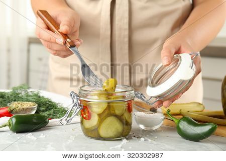 Woman Taking Pickled Cucumber From Jar At Table In Kitchen, Closeup View