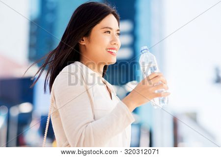 lifestyle and people concept - young asian woman drinking water flom plastic bottle in city