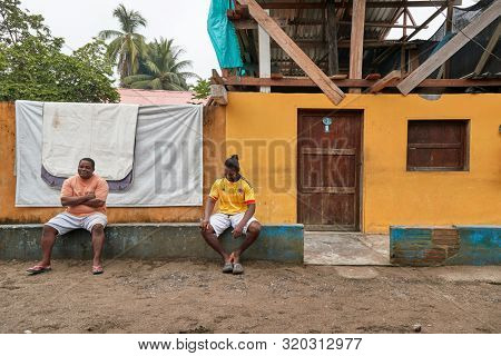 TERMALES, NUQUI, COLOMBIA - APRIL 17, 2019: Villagers sitting in front of houses in a poor, Pacific coastal region of Colombia, mostly inhabited by a population of black people