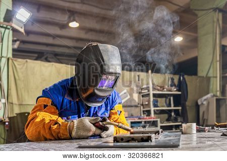 Welder At Work. Worker Welds Metal Parts. Welding Process, Sparks, Flame, Smoke. Plant For The Produ