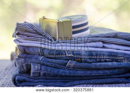 Denim Blue Jeans Stack On A Blurred Natural Background. Accessory Belt Denim. Youth Fashion.