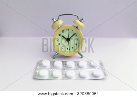 Pills Lie Next To The Alarm Clock On A Light Background. Healthcare And Medicine Concept.