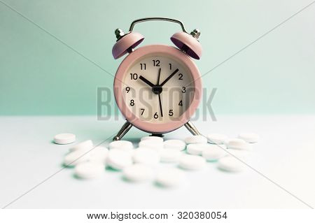 Pills Lie Next To The Alarm Clock On A Light Background. Healthcare And Medicine Concept.