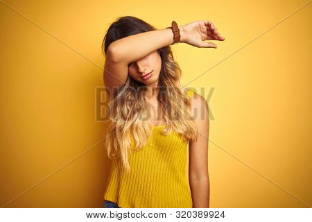 Young beautiful woman wearing t-shirt over yellow isolated background covering eyes with arm, looking serious and sad. Sightless, hiding and rejection concept