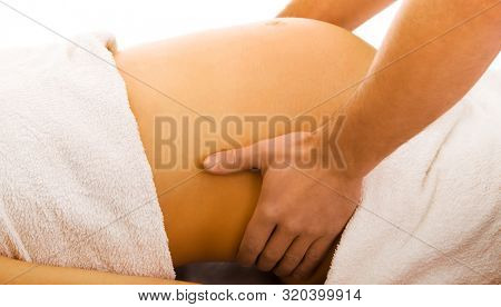 Close view on pregnant woman belly while having massage. Prenatal therapy.