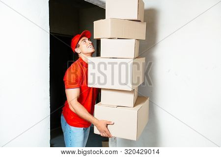Funny Friendly Delivery Man In Red Uniform Carrying Pile Of Boxes Torecently Bought Flat. He Is Hold