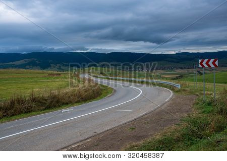 Curving Asphalt Road On The Top Of The Hill, Stormclouds Over Blue Mountains In Transylvania, Romani