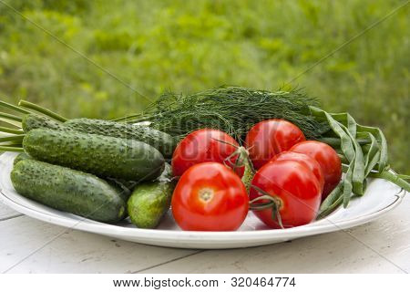 Beautiful Fresh Tasty Vegetables From The Garden Lie On A Plate On A White Table. Cucumbers, Tomatoe