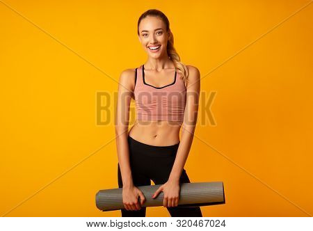 Fitness Concept. Young Woman Holding Gym Mat Smiling At Camera On Yellow Studio Background.
