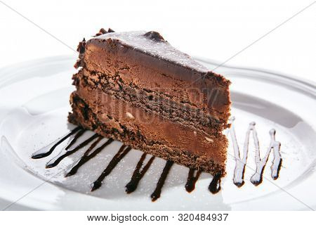 Macro photo of chocolate cake or sachertorte on white blurred background isolated. Triangular slice of brown cocoa biscuit tart decorated with chocolate sauce closeup, selective focus