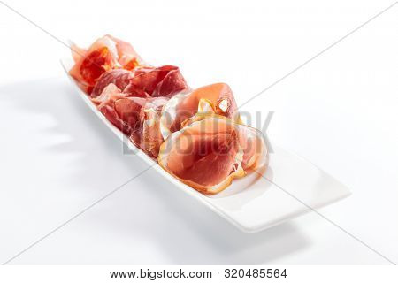 Meat assorti platter closeup. Bresaola, coppa, speck and prosciutto slices. Beef and pork, chopped on plate. Served delicious snacks. Appetizer composition isolated on white background