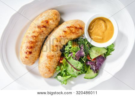 Top view of Bavarian sausages for frying with mustard sauce and mixed salad isolated. Traditional German rostbratwurst, wurst or bratwurst with fresh lettuce, rucola and chard leaves topview