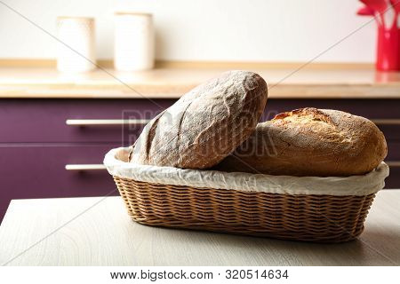 Wicker Basket With Loaves Of Tasty Fresh Bread On Wooden Table In Kitchen