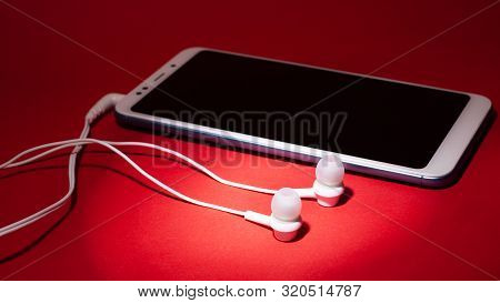 Concept: Listen To Music From The Phone.smartphone With White Headphones On A Red Background.mobile 