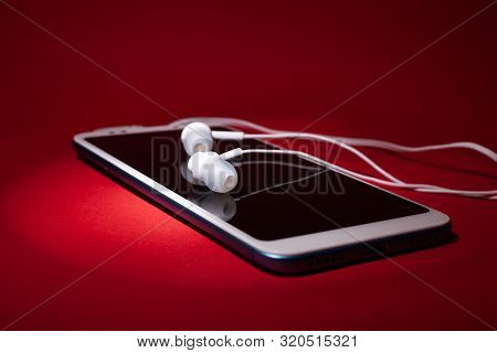 Concept: Listen To Music From The Phone With Headphones On A Red Background Close Up.