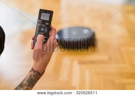 Close up of man hands controling automatic vacuum cleaner using electronic control of the mopping robot