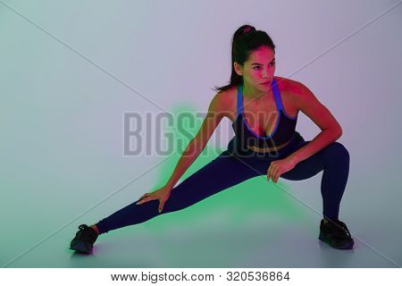 Photo of amazing beautiful young sports woman posing isolated with led flash lights make stretching exercises.