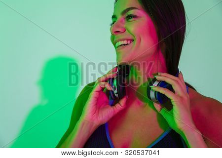 Image of cheerful optimistic young strong fitness woman isolated with led flash lights listening music with headphones.