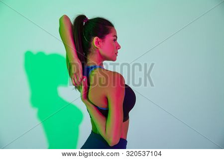 Picture of young serious sports woman posing isolated with led flash lights make stretching exercise for arms.