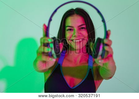 Image of beautiful smiling optimistic young strong fitness woman isolated with led flash lights give you a headphones.