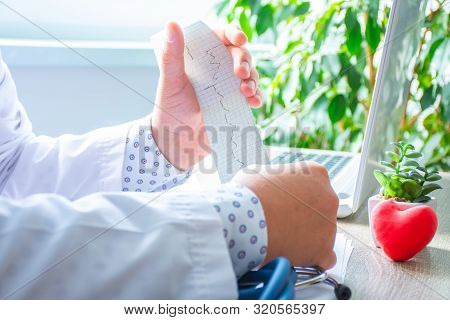 Doctor In Office At Desk With Laptop During Patient Admission Scans Paper Tape With Printed  Result 