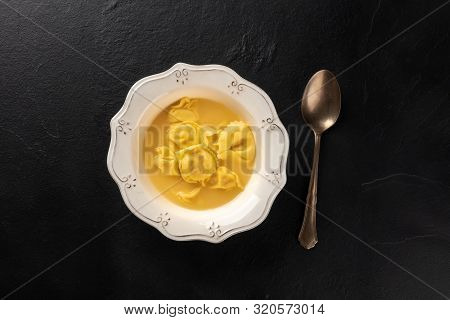 Italian Tortellini Served With Broth, Shot From Above On A Black Background With A Spoon And A Place