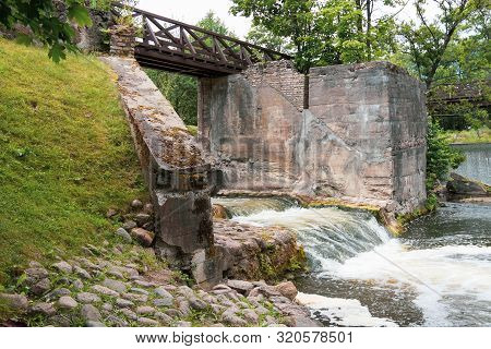 Wooden Bridge Over The River Vilia In Vilnius With A Waterfall In The Park Belmonto.