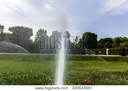 Automatic Sprinkler System Watering The Lawn On A Background Of Green Grass And Trees. Smart Garden 