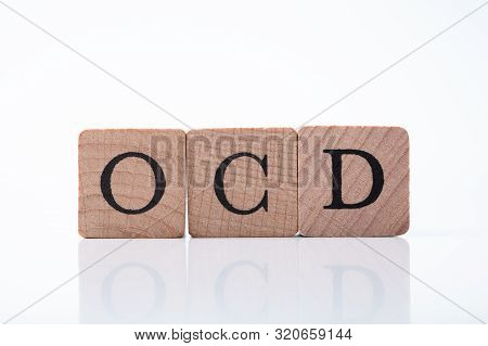 Close-up Of Ocd Text On Wooden Block Over Reflective Desk