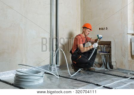 The Worker Is Installing A Pipe For The Warm Floor In The Apartment. He Is An Expanding Pipe.