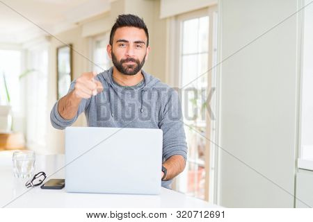 Handsome hispanic man working using computer laptop pointing with finger to the camera and to you, hand sign, positive and confident gesture from the front