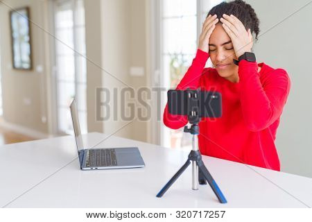 Young african american woman doing video call using smartphone camera suffering from headache desperate and stressed because pain and migraine. Hands on head.