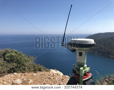 Gnss Base Receiver Stands On The Tripod At The Hill Top Against Sea At The Background.