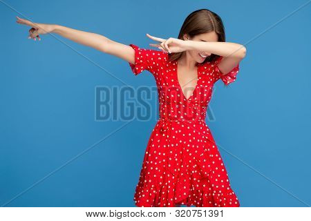 Young Woman With Bright Smile In Red Casual Dress Dubbing Over Blue Background.