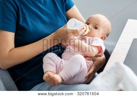 family, babyhood and people concept - close up of mother feeding baby with milk formula from bottle