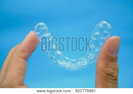 Hand Holding Clear Plastic Retainer Teeth That Isolated On Blue Sky Background. It's An Equipment Fo