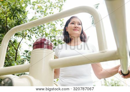 Positive Active Pretty Middle-aged Vietnamese Woman Jogging On Public Threadmill In Local Park