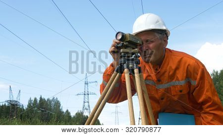 Aged Surveyor Looks Through Dumpy Level Under Power Lines