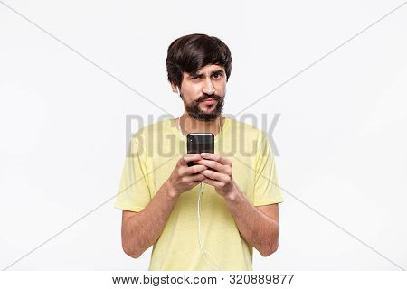Handsome Brunet Bearded Man With Whiskers In A Yellow Tee Holding Smartphone Expressing Emotion Of D