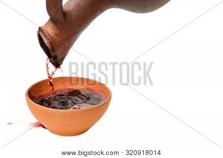A Red Wine Is Pouring From Traditional Georgian Wine Jug In To The Clay Cup, Isolated White Backgrou