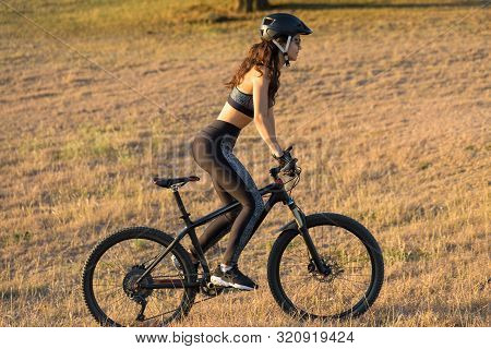 Girl On A Mountain Bike On Offroad, Beautiful Portrait Of A Cyclist At Sunset, Fitness Girl Rides A 